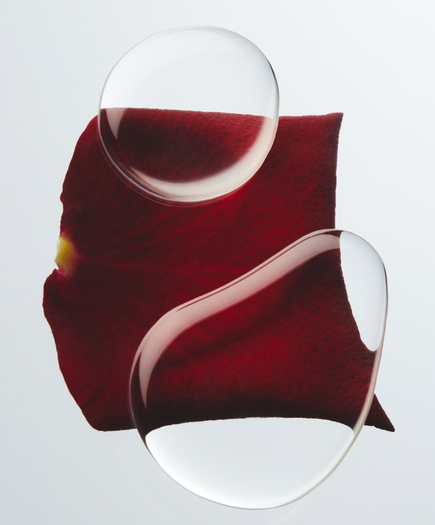 A dark red petal beneath two suspended drops of water