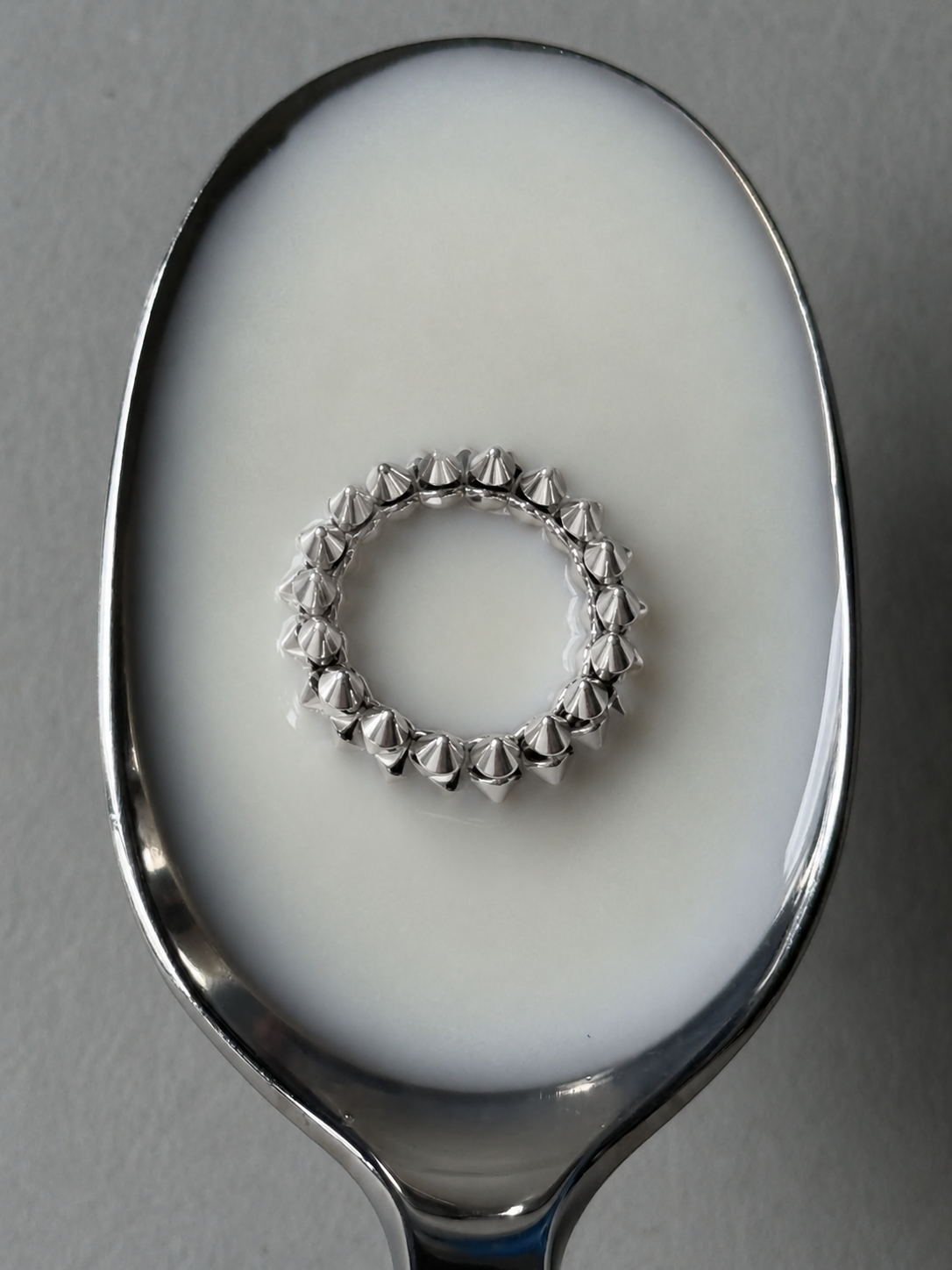 Studded silver ring resting in a spoon of milk, seen from above